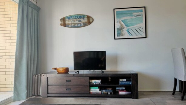Un salon avec un téléviseur posé sur un meuble en bois, un panneau d’accueil et un tableau encadré accroché au mur.