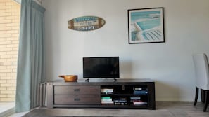 A living room with a TV on a wooden cabinet, a welcome sign, and a framed picture on the wall.