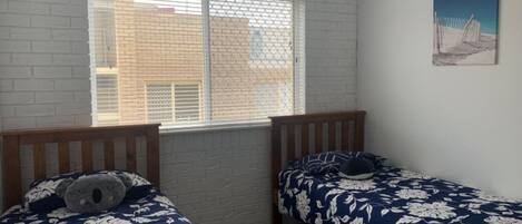 Quarto com duas camas, janela com persianas, parede de tijolos e um quadro na parede.