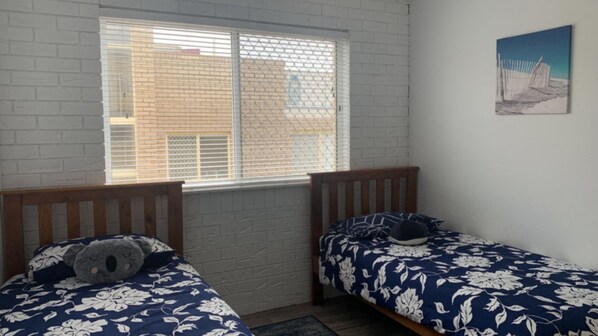 Una habitación con dos camas, una ventana con persianas, una pared de ladrillo y un cuadro en la pared.