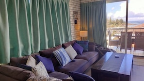Una sala de estar con sofá, cojines, una mesita de centro y vistas al exterior.