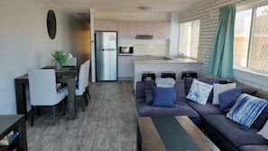 A compact living space with a kitchenette, a dining area, and a seating area with a sofa and cushions.