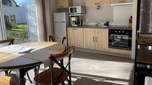 A modern kitchen with wooden cabinets, a microwave, a stove, and a dining area with a table and chairs. - Les Cottages du golf 2/3 (LE TRONCHET)