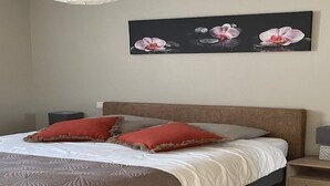 A bedroom with a bed, pillows, a nightstand, and a wall-mounted artwork. - Les Cottages du golf 2/3 (LE TRONCHET)