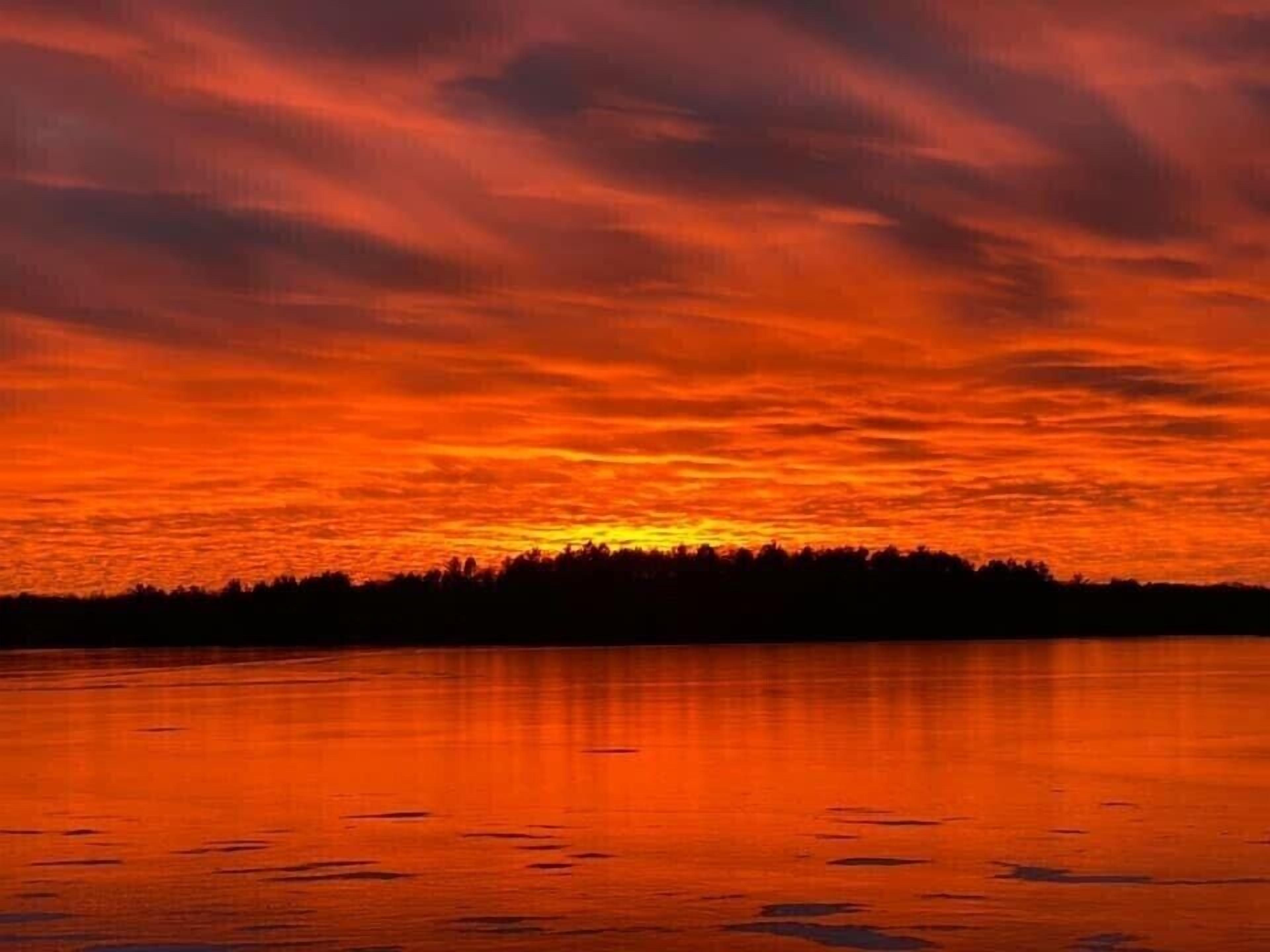 A sunset over a calm lake with a forest silhouette in the distance.