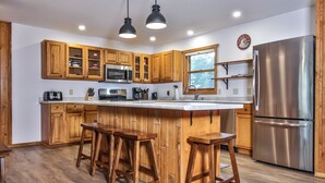 A modern kitchen with wooden cabinets, a stainless steel refrigerator, and a large island with stools. - God’s Country Minocqua, Wi. - “Up North” @ Back Bay Cabins on Lake Shishebogama  (Minocqua)
