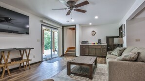 A modern living room with a flat-screen TV, a ceiling fan, a wooden coffee table, a sofa, and a kitchen area with cabinets and a microwave. - God’s Country Minocqua, Wi. - “Up North” @ Back Bay Cabins on Lake Shishebogama  (Minocqua)