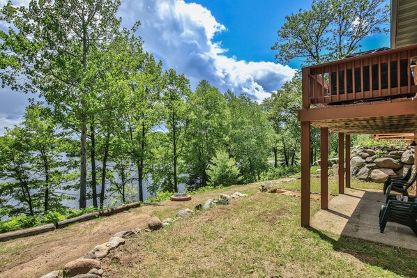 A lakeside deck with a stone pathway leading to a seating area, surrounded by trees and a view of the lake. - God’s Country Minocqua, Wi. - “Up North” @ Back Bay Cabins on Lake Shishebogama (Minocqua)