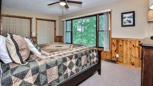A bedroom with a large bed, wooden walls, a ceiling fan, and a window with a view of trees. - God’s Country Minocqua, Wi. - “Up North” @ Back Bay Cabins on Lake Shishebogama  (Minocqua)