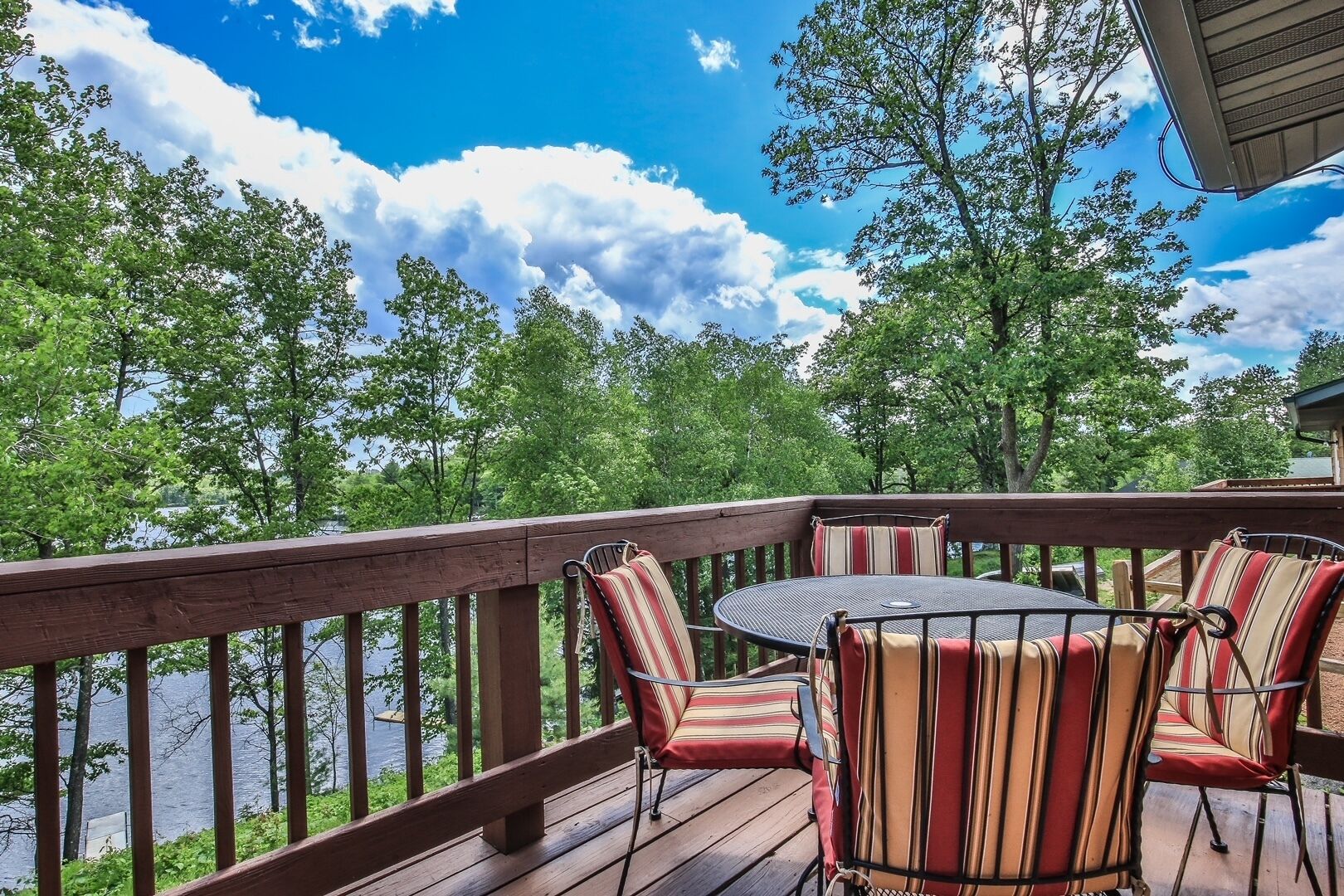 A wooden deck with a table and chairs, overlooking a body of water and surrounded by trees.
