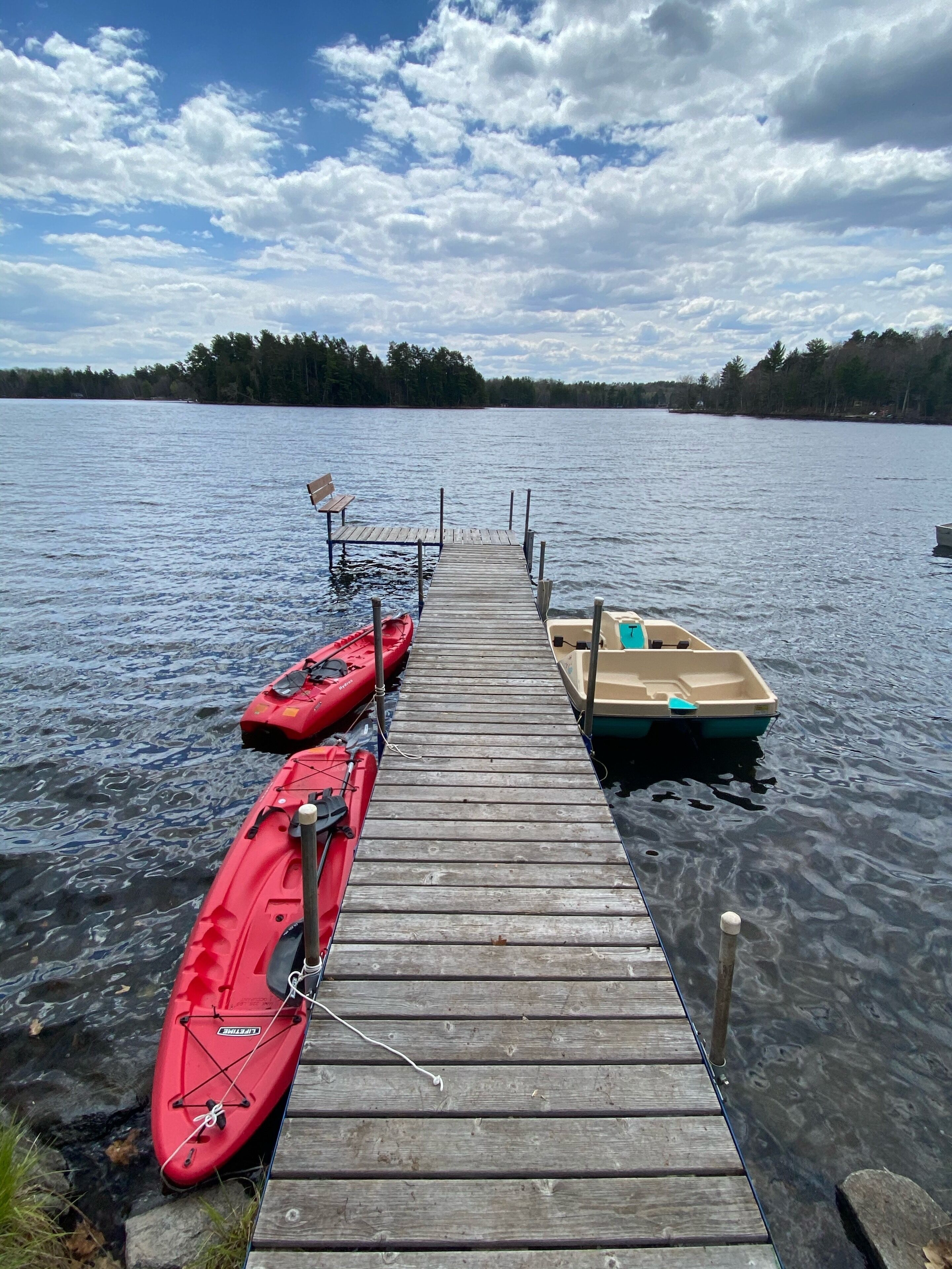 Un muelle de madera se extiende sobre aguas tranquilas, con kayaks y un pequeño bote amarrados al final.