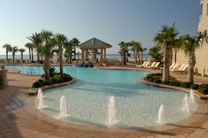 Relax by the pool surrounded by palm trees and lounge chairs, with a gazebo nearby for shade.