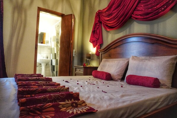 A neatly made bed with a floral bedspread, red pillows, and a wooden headboard.