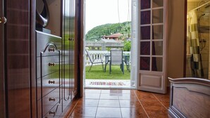 Uma porta aberta dá para uma varanda com vista para uma casa e vegetação.