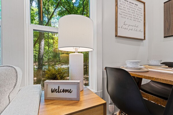 Un coin repas avec une table en bois, des chaises noires, une lampe blanche et une pancarte « Bienvenue ».