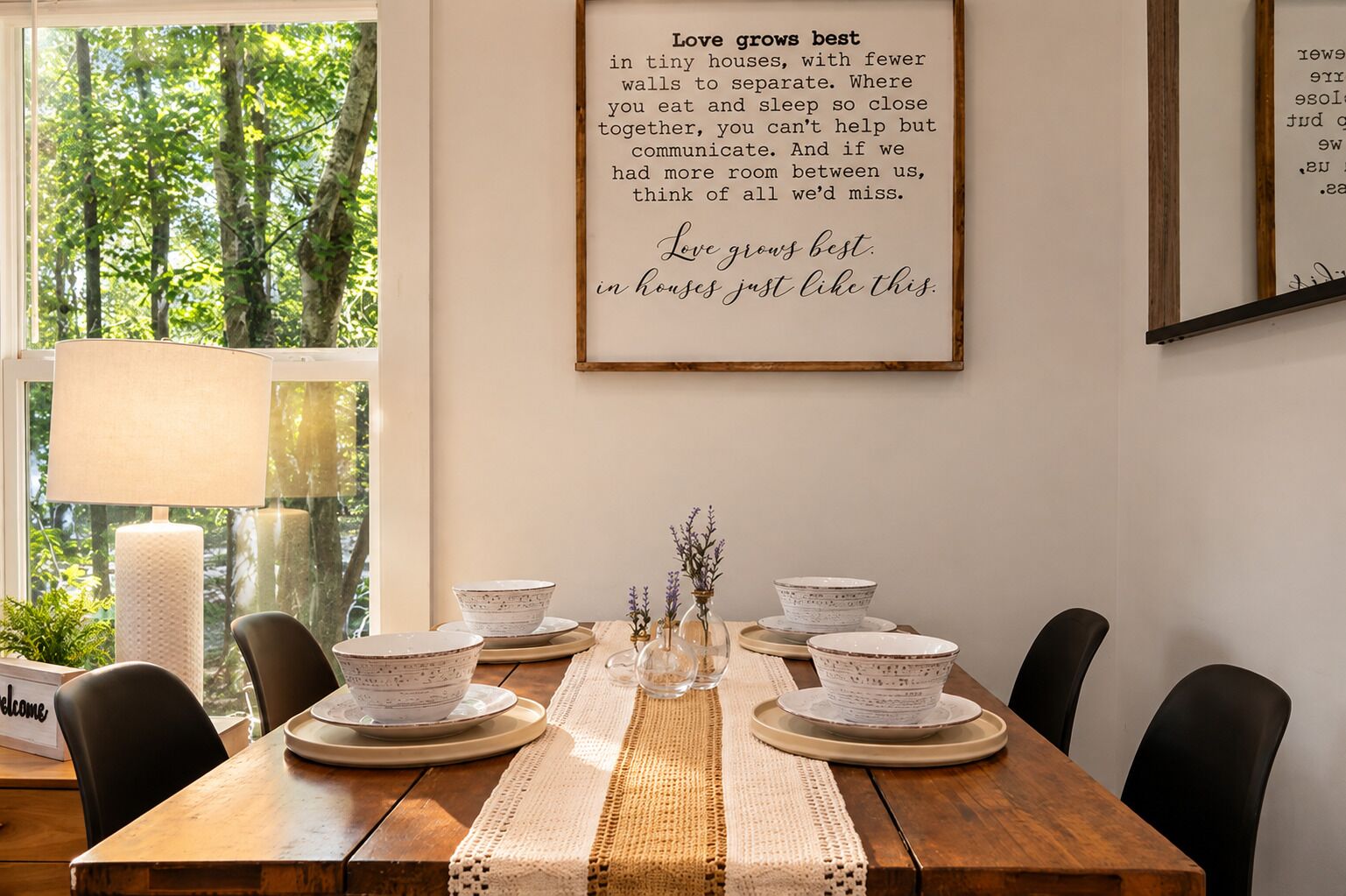 Un coin repas avec une table en bois dressée pour quatre personnes, entourée de chaises. Un cadre contenant une citation sur l’amour est accroché au mur.