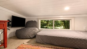 A bedroom with a bed, a bean bag, a TV, and a window with a view of greenery.