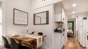 A modern kitchen with white cabinetry, a wooden dining table with black chairs, and a coffee maker on the counter.