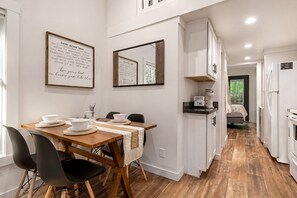 Una cocina moderna con armarios blancos, una mesa de comedor de madera con sillas negras y una cafetera sobre la encimera.