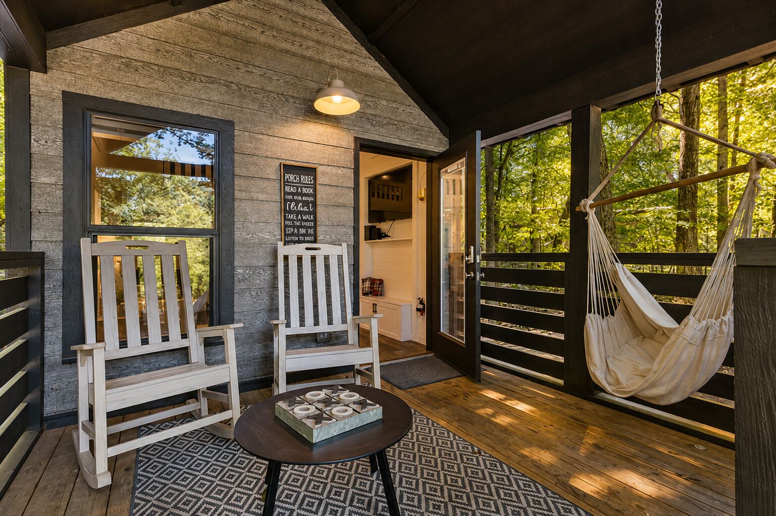 A wooden deck with two white chairs, a hanging hammock, and a table with a decorative box.