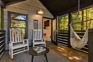 A wooden deck with two white chairs, a hanging hammock, and a table with a decorative box.