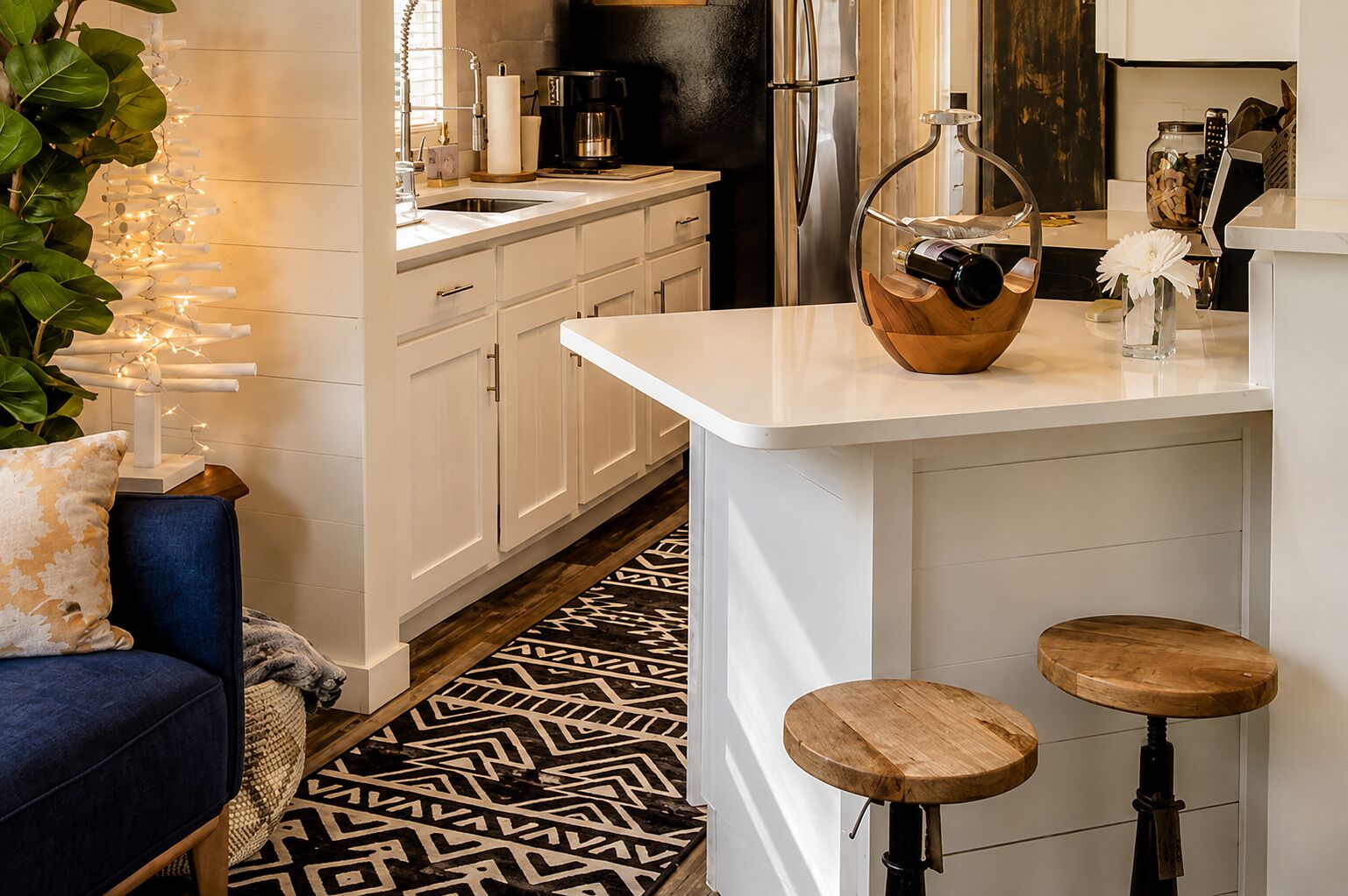 Une cuisine moderne avec des meubles blancs, un réfrigérateur noir et un tabouret de bar en bois.