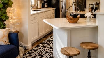 A modern kitchen with white cabinetry, a black refrigerator, and a wooden bar stool.