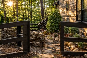 A wooden pathway leading to a house surrounded by a forest.