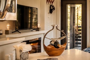 Una cocina moderna con chimenea, un soporte para botellas de vino con forma de cuenco de madera y un televisor sobre la encimera.