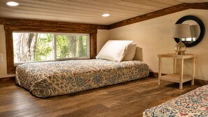A bedroom with a bed, a bedside table with a lamp, and a window with a view of trees. - The Woods at The Retreat at Deer Lick Falls (Monteagle)