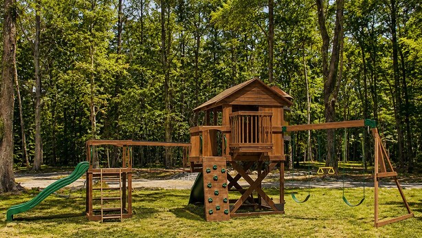 A wooden play structure with a slide and swings in a grassy park area. - The Woods at The Retreat at Deer Lick Falls (Monteagle)