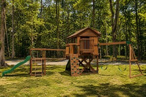 Estructura de juego de madera con tobogán y columpios en un parque con césped.