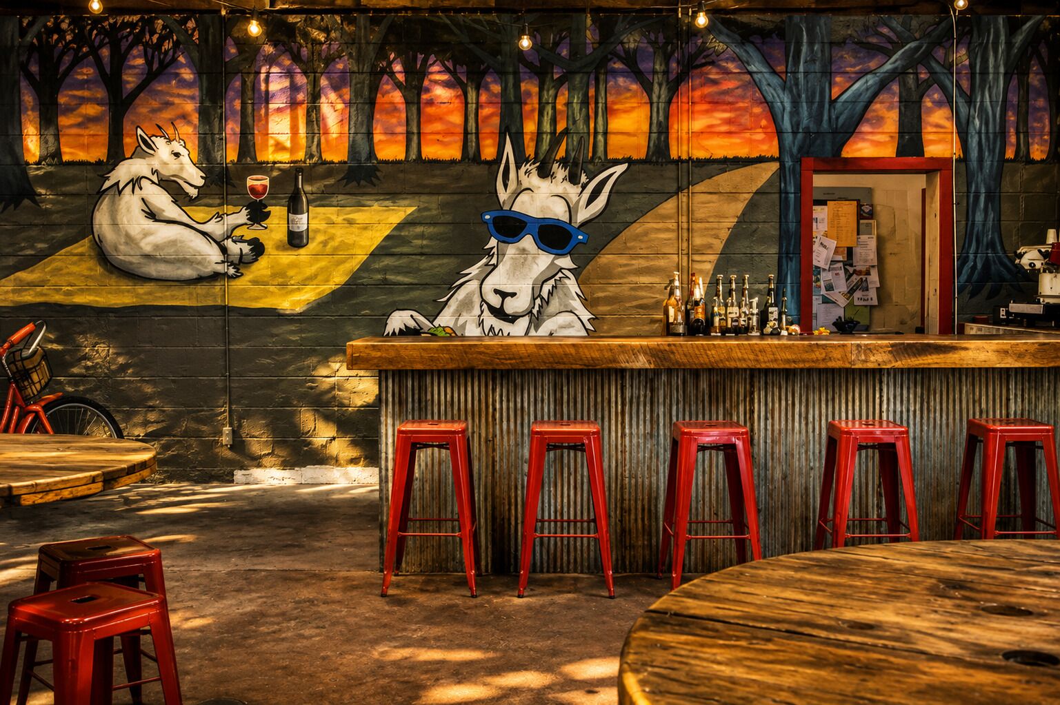 Un bar orné d’une fresque représentant un loup et un cheval, avec des tabourets rouges et un comptoir en bois.