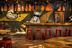 Un bar orné d’une fresque représentant un loup et un cheval, avec des tabourets rouges et un comptoir en bois.