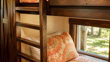 Uma cama de beliche com janela, um travesseiro estampado e uma escada de madeira.