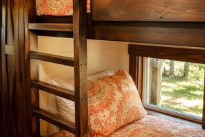 Una cama individual en literas con ventana, almohada estampada y escalera de madera.