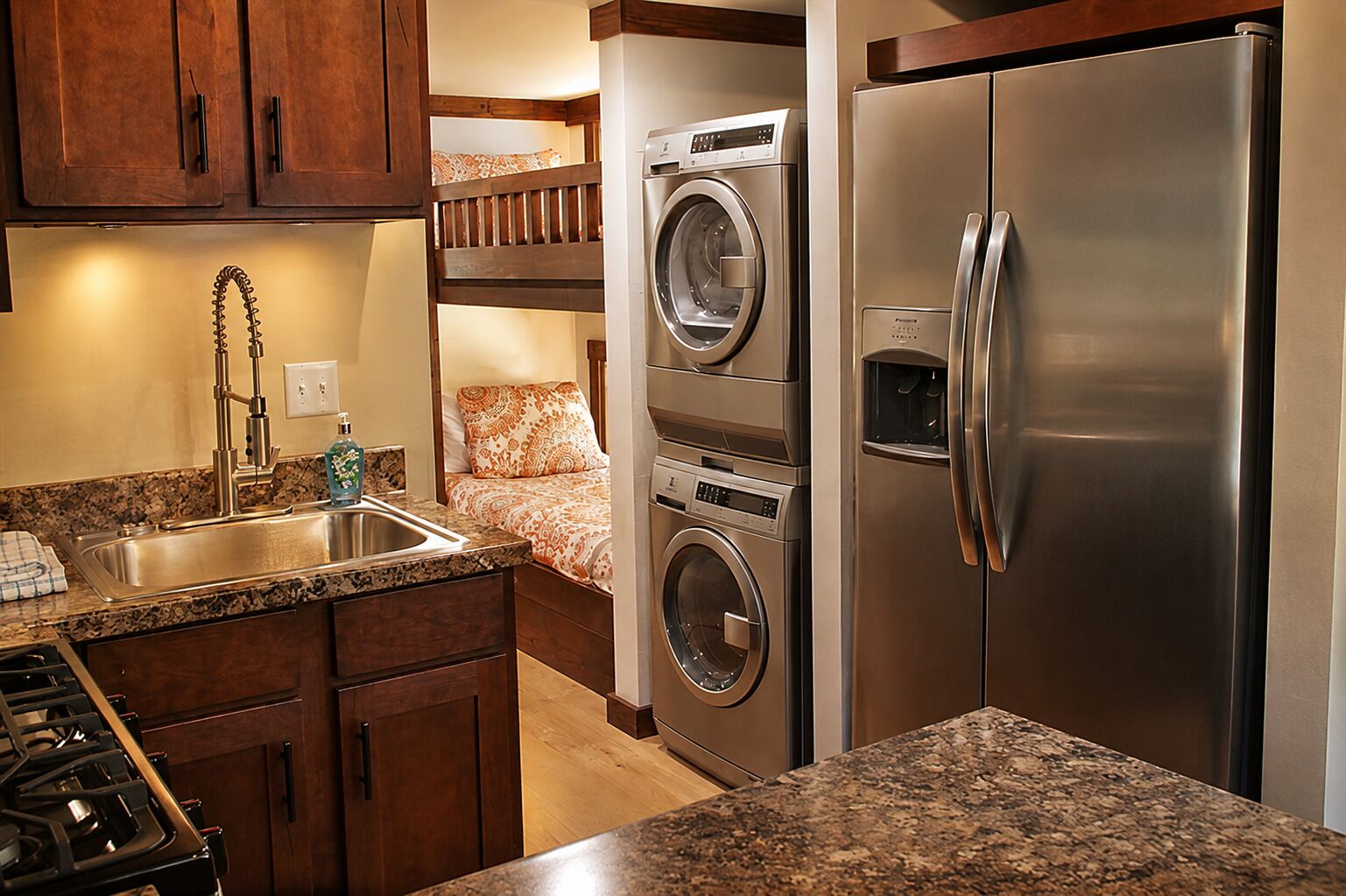 A compact kitchen with a built-in washer and dryer, a stainless steel refrigerator, and a granite countertop.