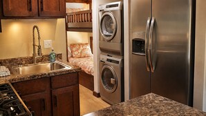 A compact kitchen with a built-in washer and dryer, a stainless steel refrigerator, and a granite countertop. - The Woods at The Retreat at Deer Lick Falls (Monteagle)