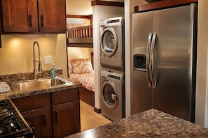 A compact kitchen with a built-in washer and dryer, a stainless steel refrigerator, and a granite countertop. - The Woods at The Retreat at Deer Lick Falls (Monteagle)