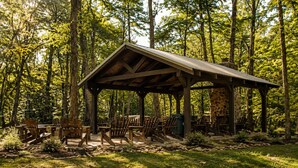 A covered pavilion with wooden chairs and a stone fireplace, surrounded by a forest. - The Woods at The Retreat at Deer Lick Falls (Monteagle)