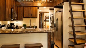 A kitchen with wooden cabinets, stainless steel appliances, a granite countertop, and a wooden ladder shelf. - The Woods at The Retreat at Deer Lick Falls (Monteagle)