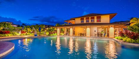A hotel with a swimming pool, outdoor seating, and a starry night sky.