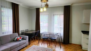 A modern living room with a sofa, dining table, chairs, and a kitchen area. - Anemo Suite (Çaykara)
