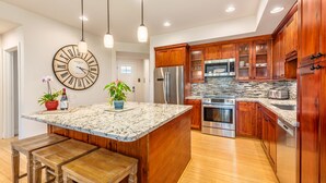 A modern kitchen with wooden cabinets, stainless steel appliances, and a marble island with bar stools.