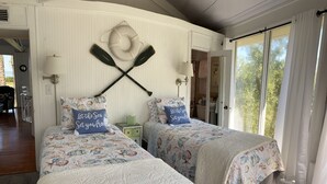 Habitación con dos camas, cada una con colcha y almohadas de temática náutica. Se observan dos remos colgados en la pared sobre las camas, y una pequeña mesita de noche verde con una lámpara.