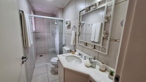 Casa de banho moderna com cabine de duche em vidro, lavatório branco e espelho grande com detalhes decorativos.