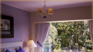 A bedroom with a bed, a nightstand, a lamp, and a window with curtains. - Pousada Mar Deny Campos (Campos do Jordão)