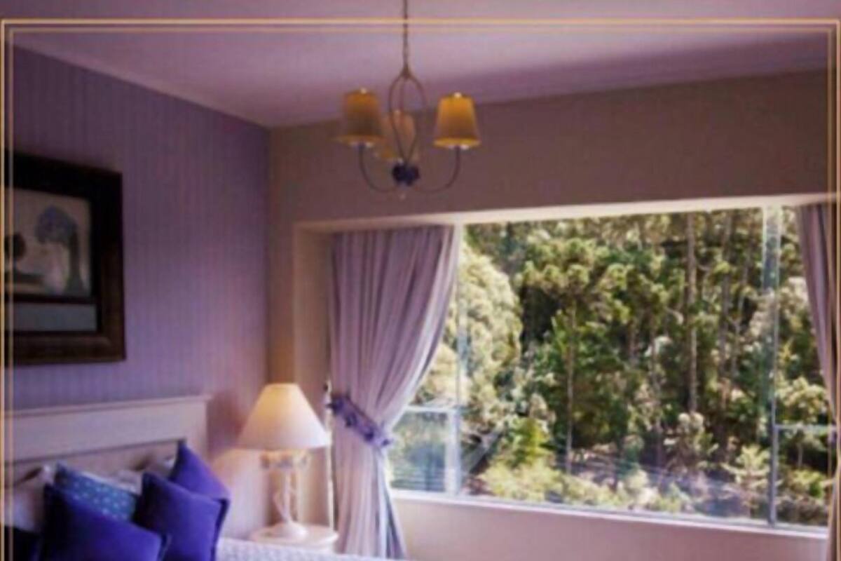 Ein Schlafzimmer mit Bett, Nachttisch, Lampe und einem Fenster mit Vorhängen.