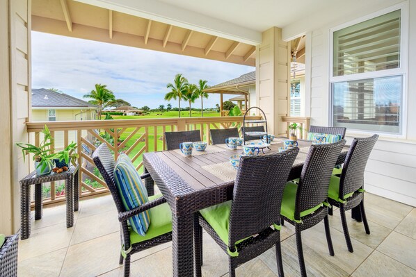 Une terrasse couverte avec une table à manger pour quatre personnes, entourée de chaises en osier avec des coussins verts.