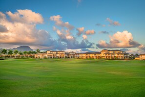 A golf course with a row of multi-story buildings in the background. - Pili Mai Family Condo 10B, 4 Bedrooms, 3.5 bath, AC Lanai Dining w/ Sunsets! (Koloa)